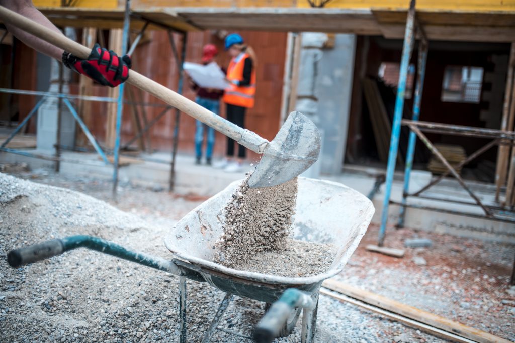 In eine Schubkarre wird Schotter geschaufelt