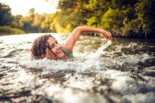 Frau schwimmt im Bach und lächelt dabei