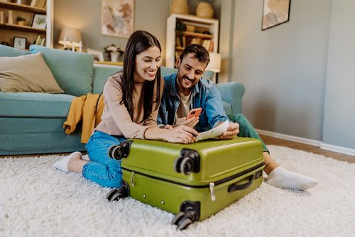Paar bereitet sich auf den Urlaub vor und sitzt mit dem Koffer auf dem Boden und scannt die Boarding Tickets